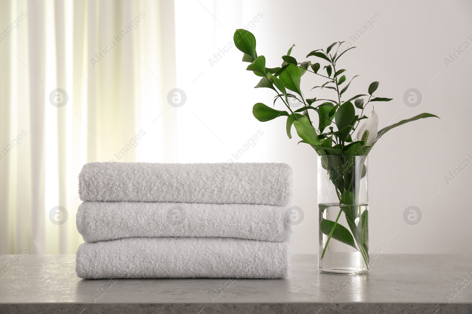 Photo of Fresh towels and green branches on light grey stone table in bathroom