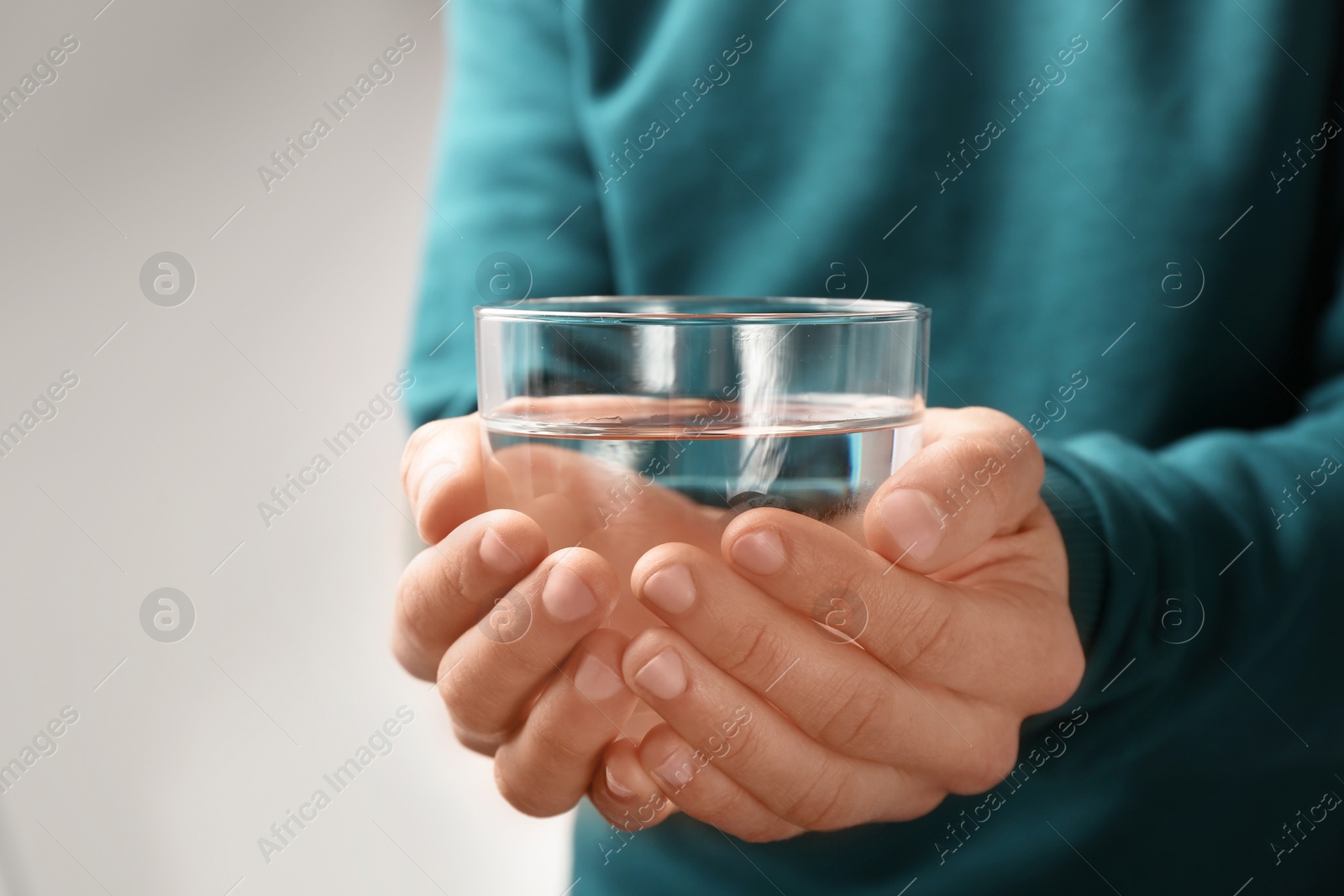 Photo of Man holding glass with fresh water against gray background, closeup