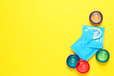 Colorful condoms on yellow background, flat lay. Space for text