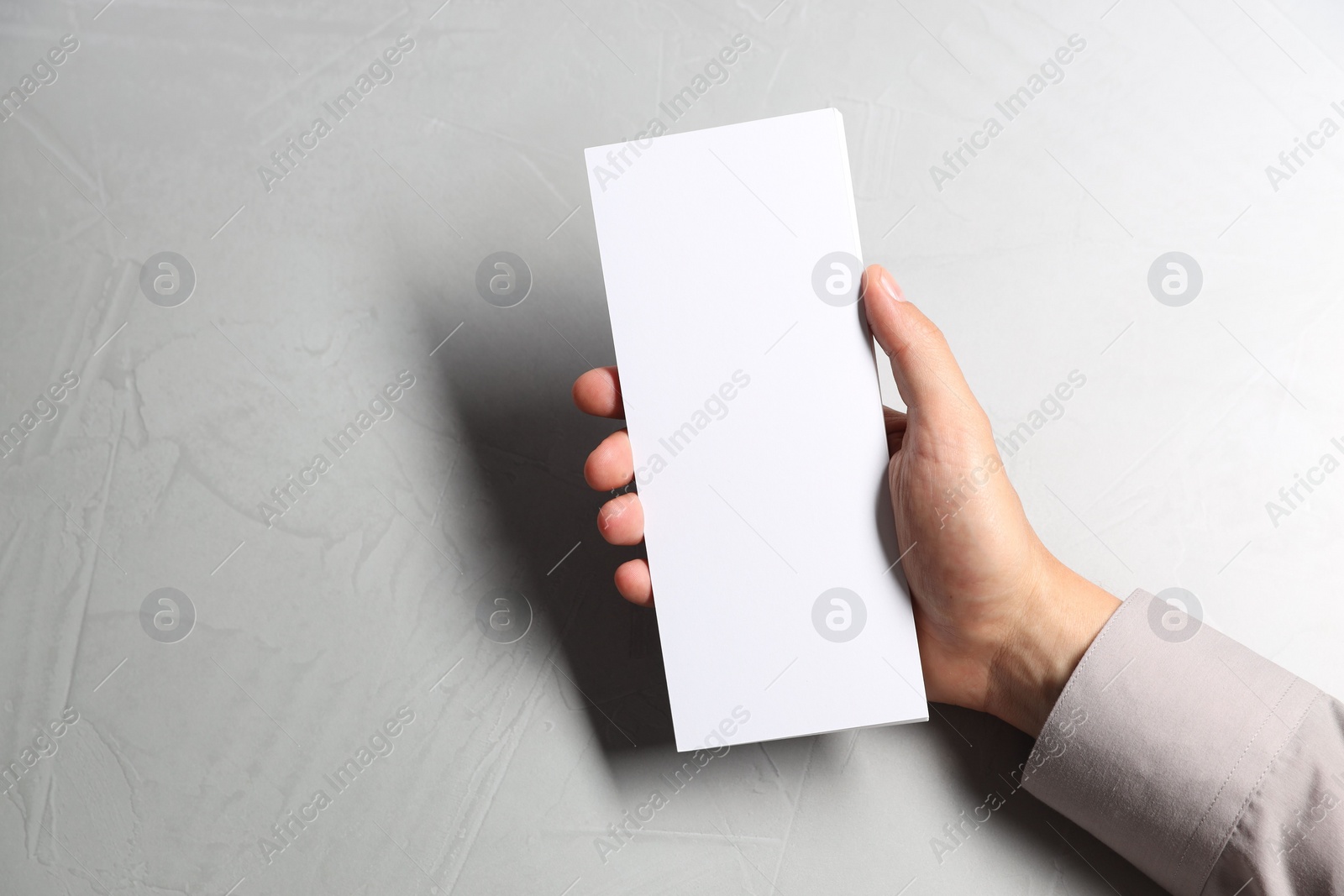 Photo of Man holding white blank card at light grey table, top view. Mockup for design