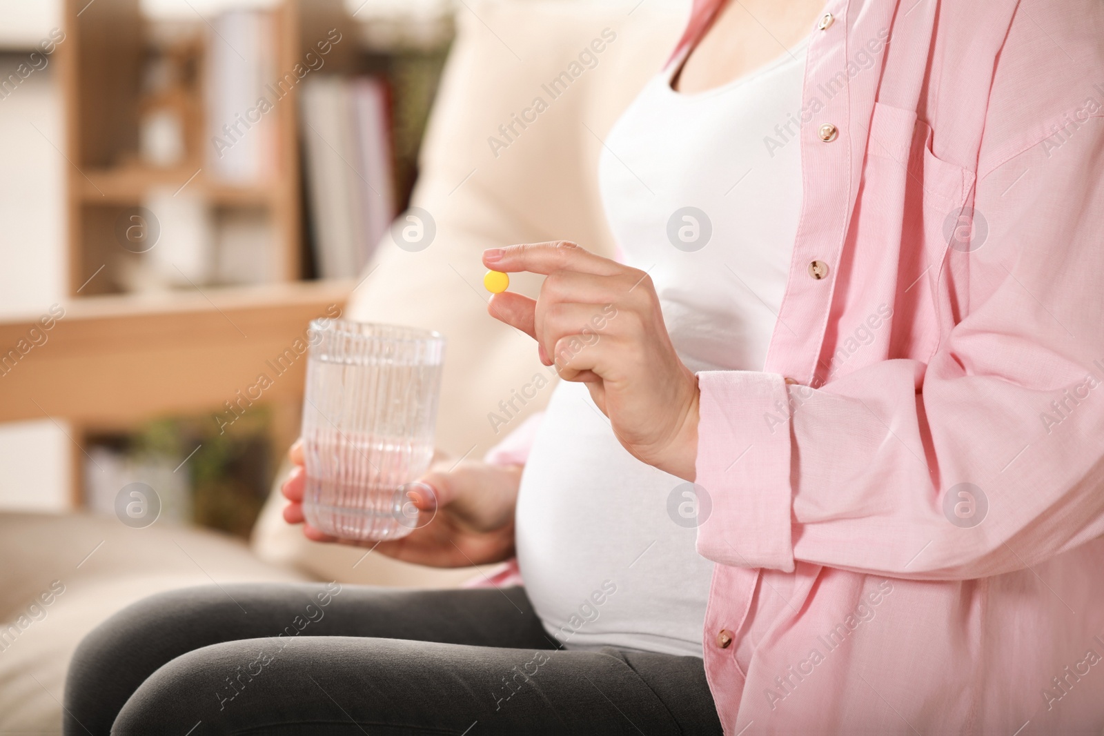 Photo of Pregnant woman holding pill and glass with water at home, closeup