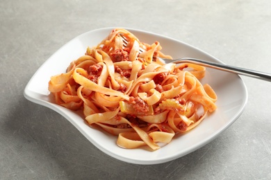 Photo of Plate with delicious pasta bolognese on grey background
