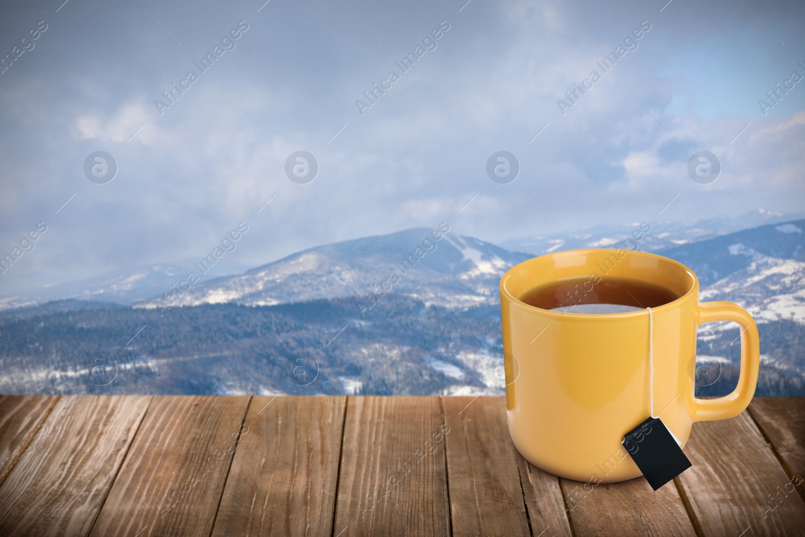 Image of Cup of hot tea on wooden table and beautiful winter landscape on background