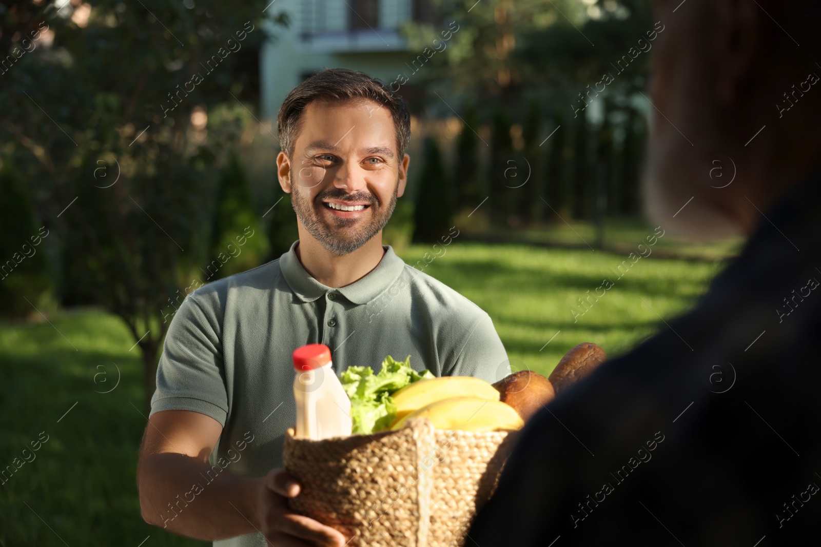 Photo of Man with wicker bag of products helping his senior neighbour outdoors