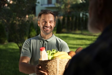 Man with wicker bag of products helping his senior neighbour outdoors