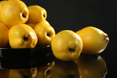 Tasty ripe quinces in bowl on black mirror surface, closeup