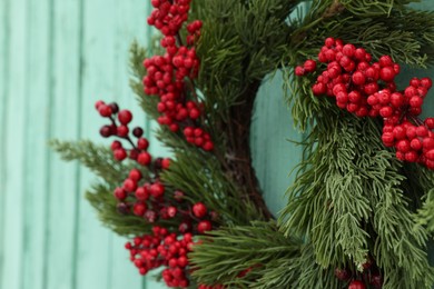 Photo of Beautiful Christmas wreath with red berries hanging on turquoise wall, closeup