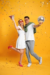 Photo of Happy couple with disco ball and confetti on yellow background
