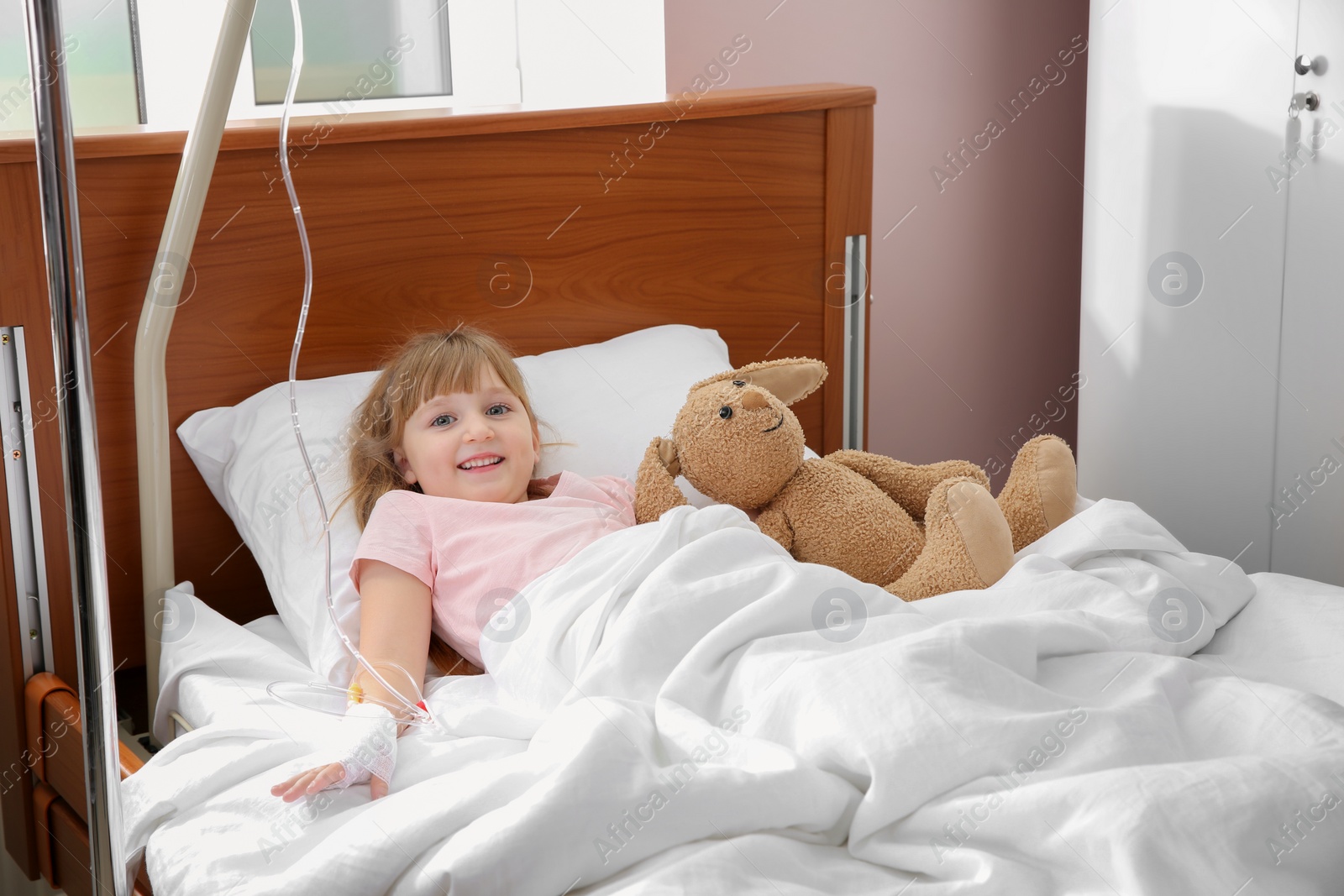 Photo of Little child with intravenous drip and toy in hospital bed