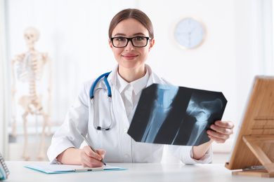 Orthopedist examining X-ray picture at desk in clinic