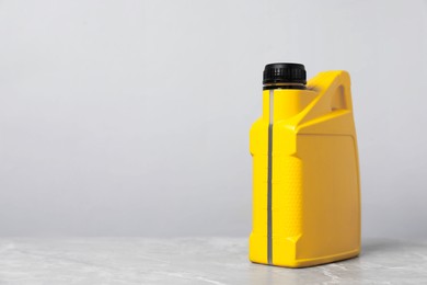 Photo of Motor oil in yellow canister on grey marble table against light background, space for text