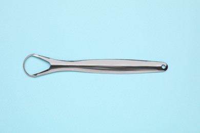 Photo of Metal tongue cleaner on light blue background, top view