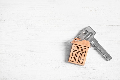 House key with trinket on white wooden table, top view. Space for text