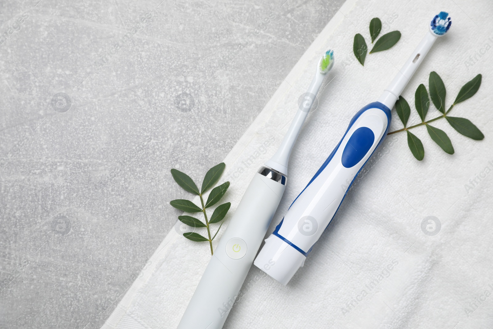 Photo of Electric toothbrushes, towel and leaves on grey textured table, top view. Space for text