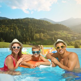 Image of Happy family in outdoor swimming pool at luxury resort and beautiful view of mountains on sunny day