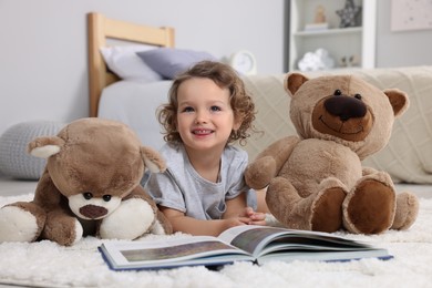 Cute little girl with book and teddy bears on floor at home