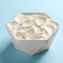 Photo of Bowl of tasty cream cheese on color background