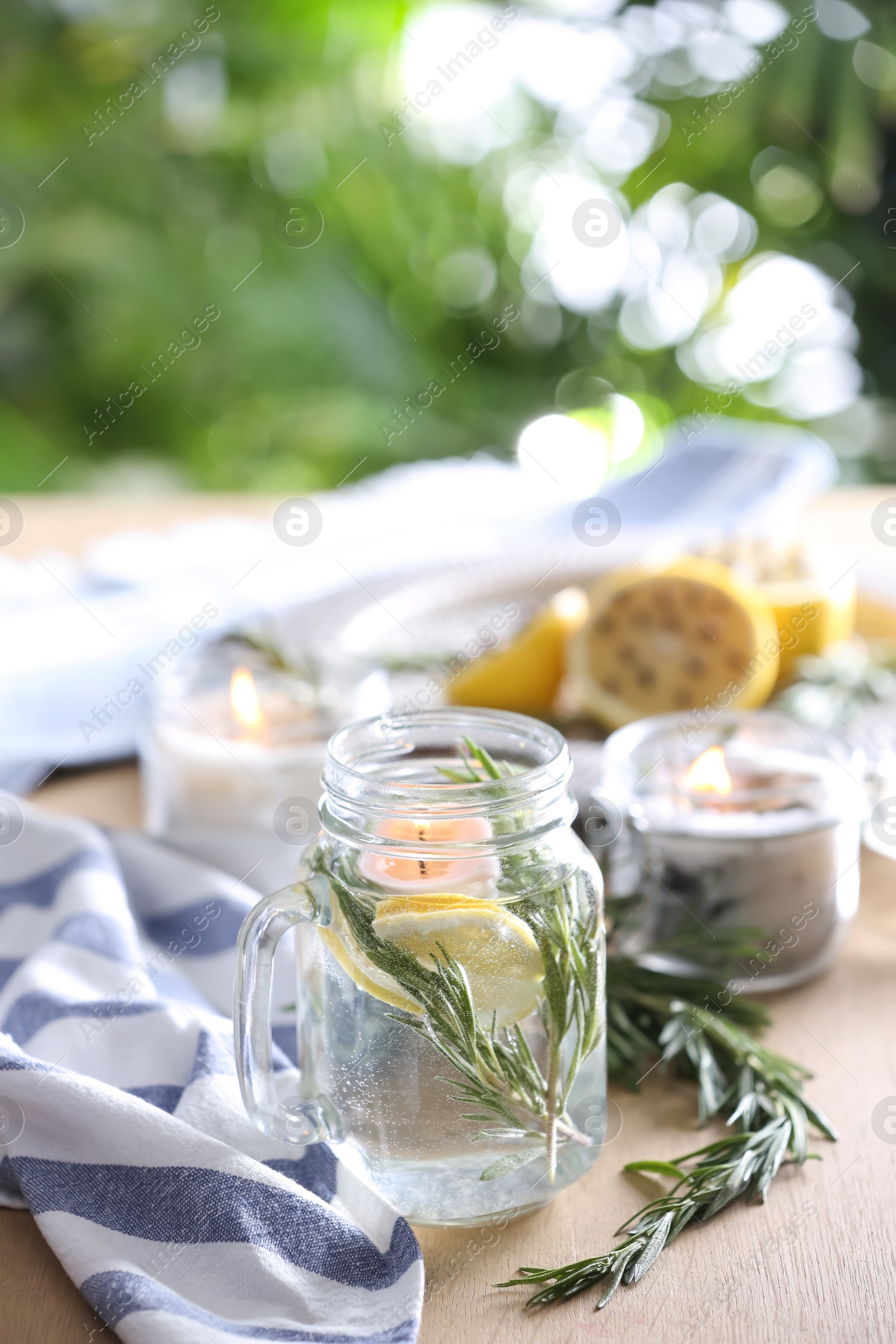 Photo of Mason jar with slice of lemon, fresh rosemary and water on wooden table outdoors. Natural homemade repellent