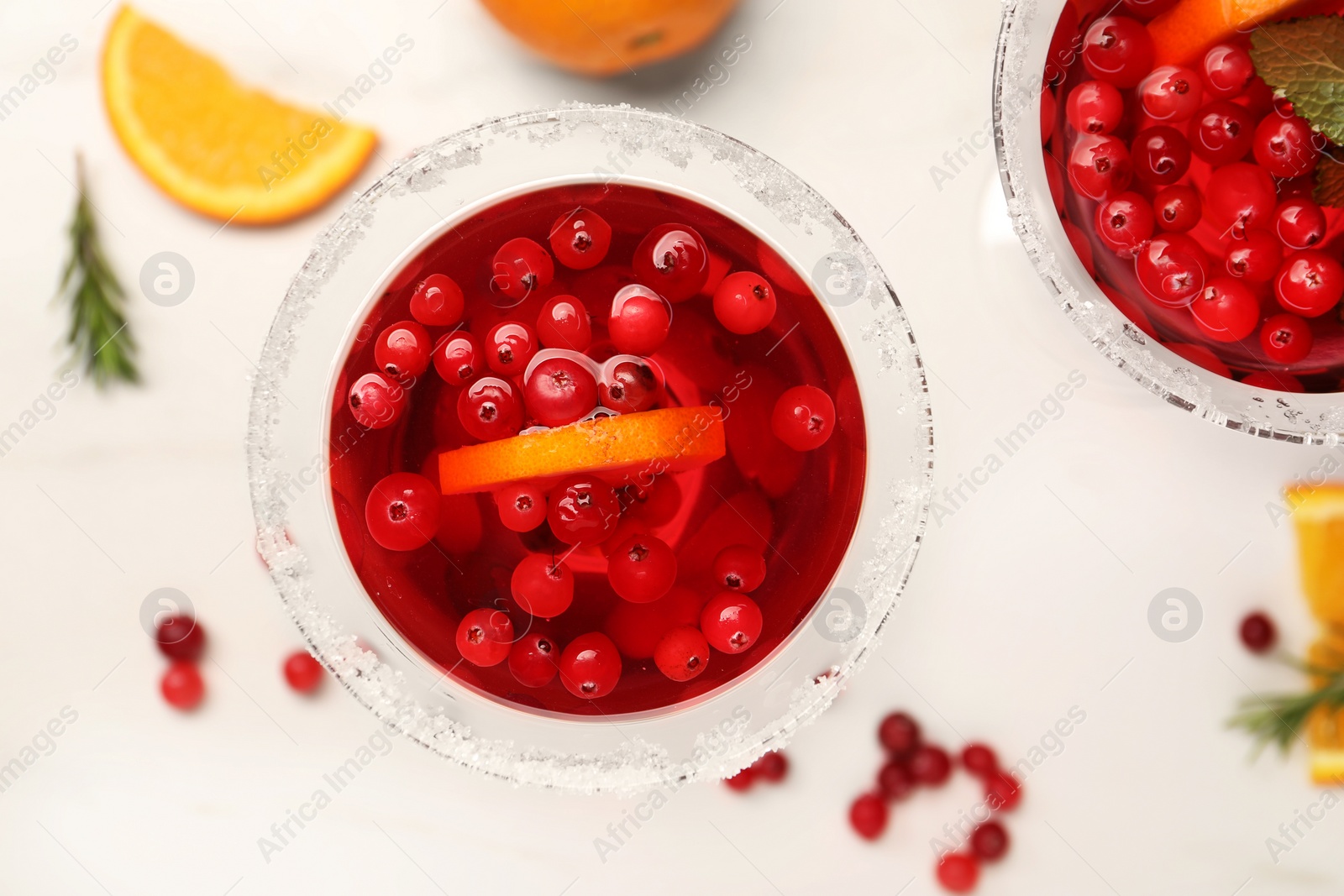 Photo of Tasty cranberry cocktail with rosemary and oranges in glasses on white table, flat lay