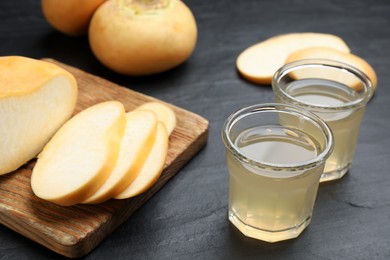 Photo of Glasses of fresh natural turnip juice, cut and whole roots on black table