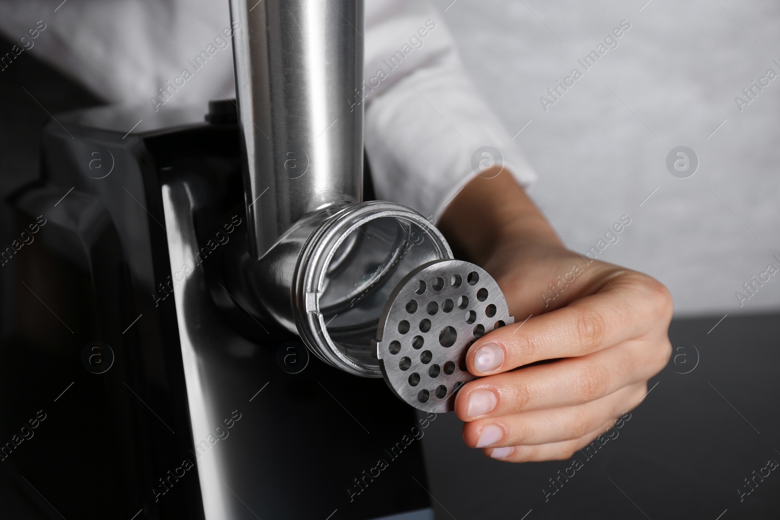 Photo of Woman assembling electric meat grinder at black table, closeup