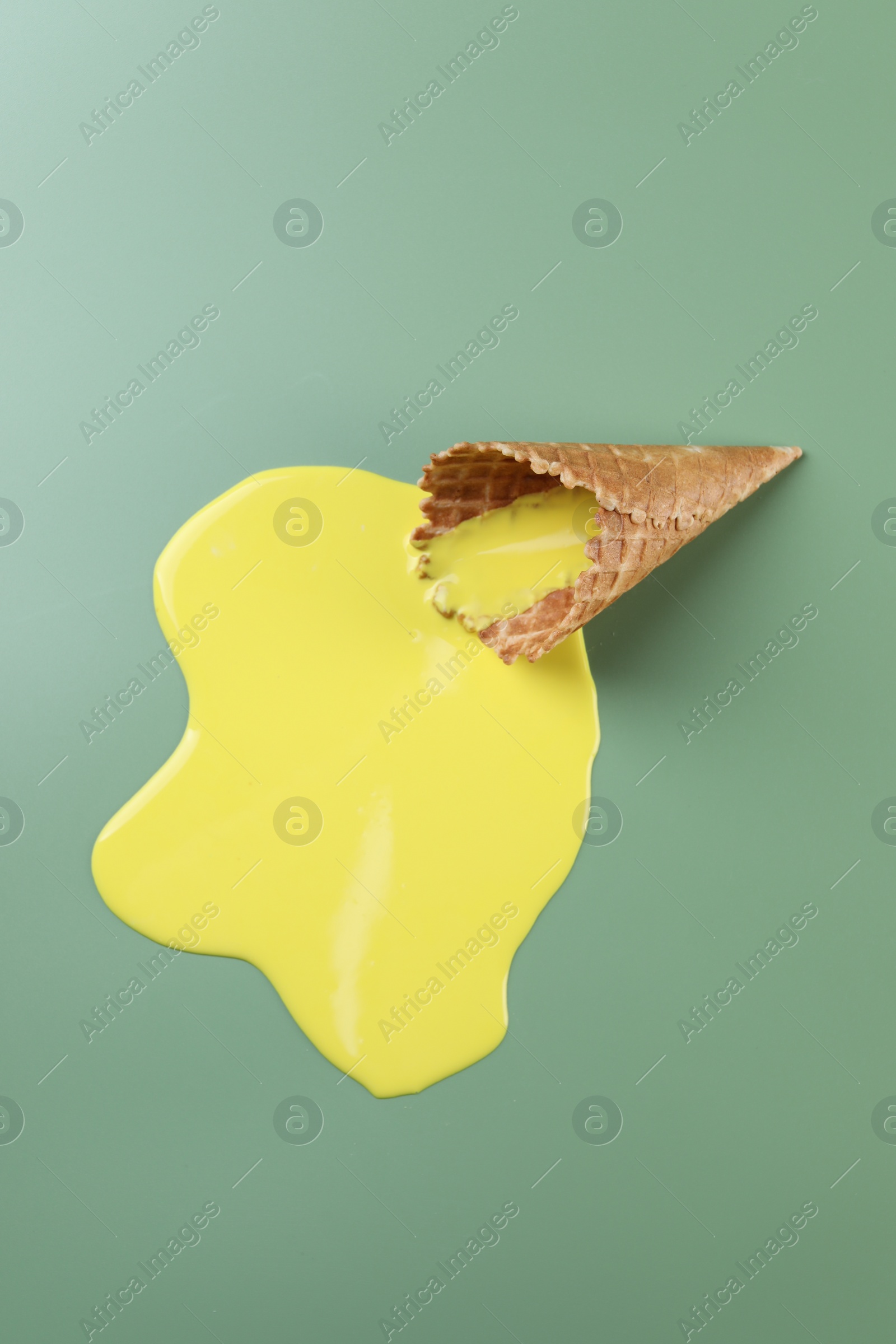 Photo of Melted ice cream and wafer cone on green background, above view