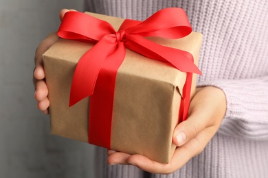 Photo of Young woman holding Christmas gift on light background, closeup