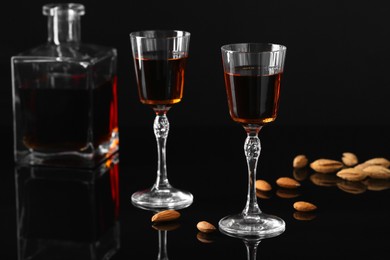 Photo of Liqueur glasses with tasty amaretto, bottle and almonds on black table, closeup