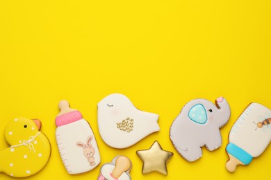 Cute tasty cookies of different shapes on yellow background, flat lay with space for text. Baby shower party