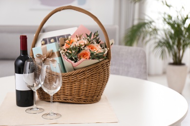 Wicker basket with gifts near bottle of wine and glasses on table indoors. Space for text