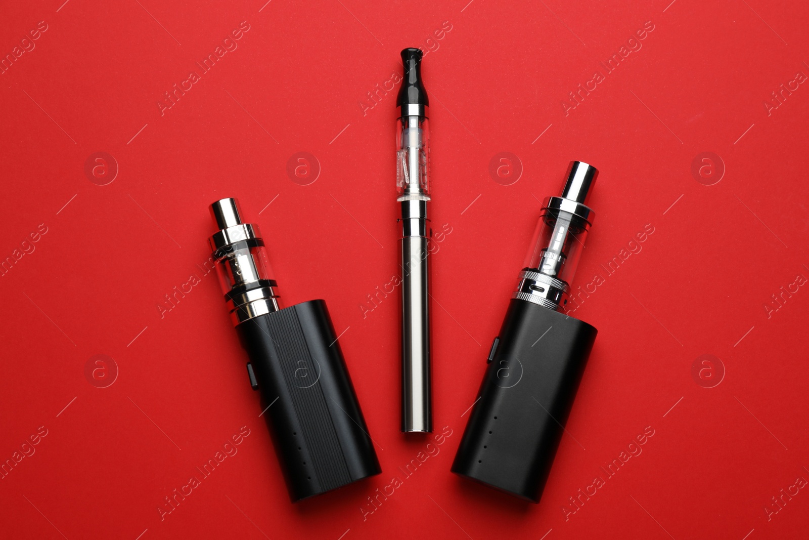 Photo of Electronic smoking devices on red background, flat lay