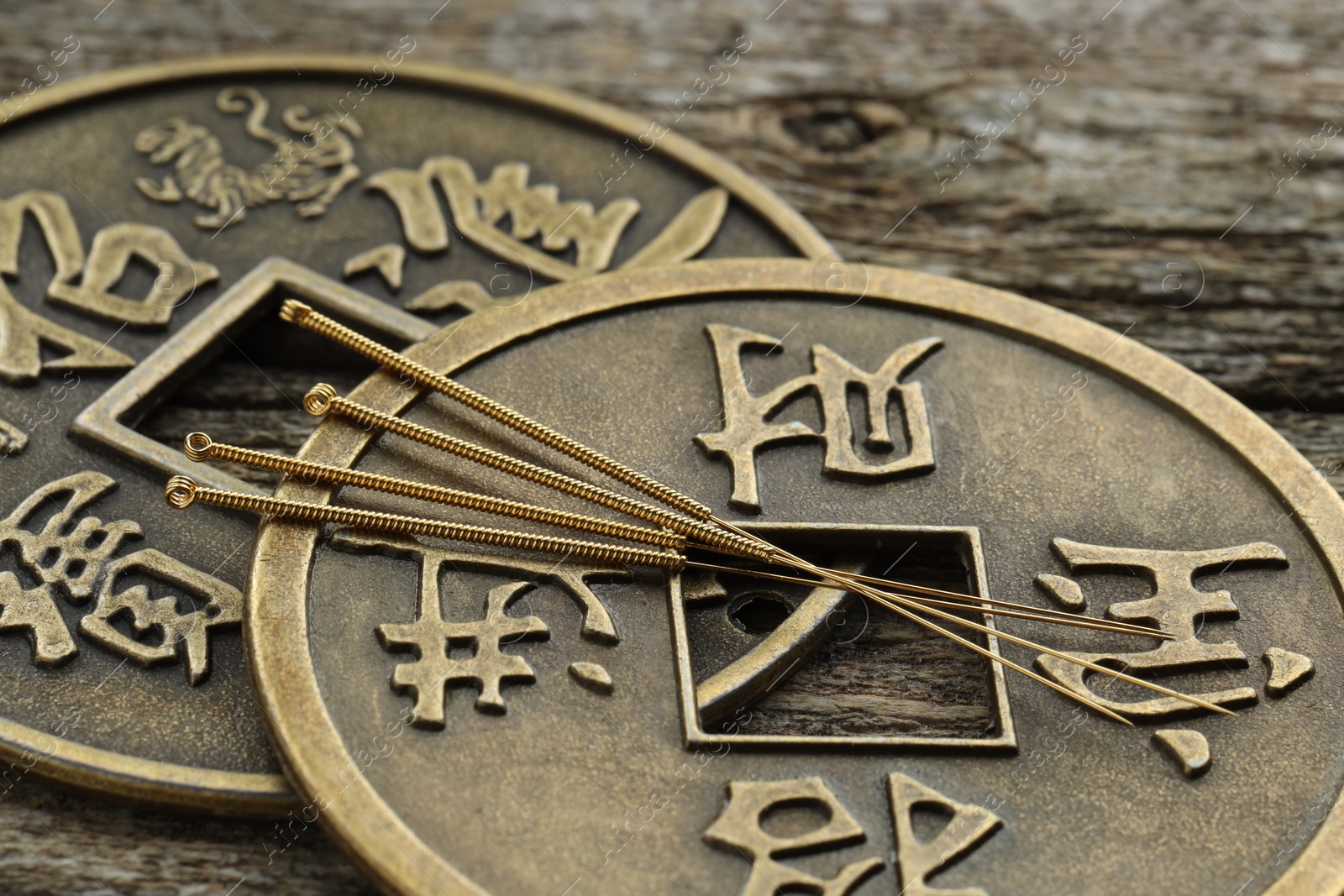 Photo of Acupuncture needles and Chinese coins on wooden table, closeup