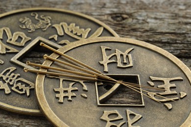 Photo of Acupuncture needles and Chinese coins on wooden table, closeup