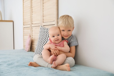 Photo of Cute boy hugging his little sister on bed at home