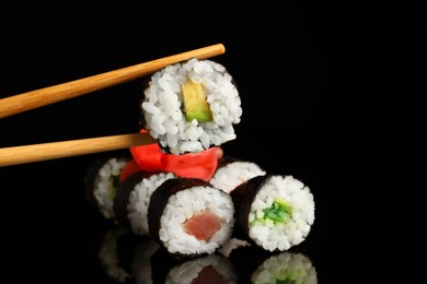 Set of delicious sushi rolls and chopsticks on black background
