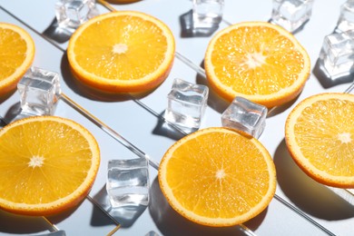 Slices of juicy orange and ice cubes on light blue background, closeup