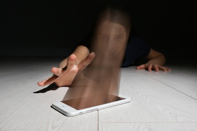 Internet or social media addiction concepts. Woman reaching out for smartphone on floor, her face absorbing by device