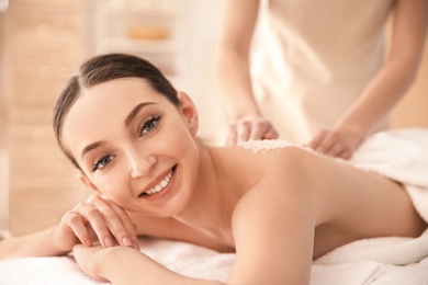 Beautiful young woman having massage with body scrub in spa salon