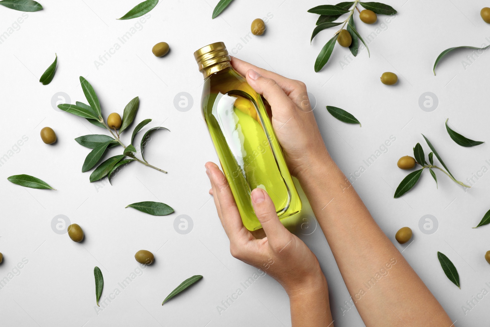 Photo of Woman holding bottle of olive oil on light background, top view