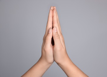 Photo of Woman holding hands clasped while praying against light grey background, closeup