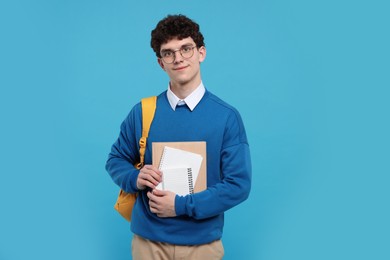 Portrait of student with backpack and notebooks on light blue background