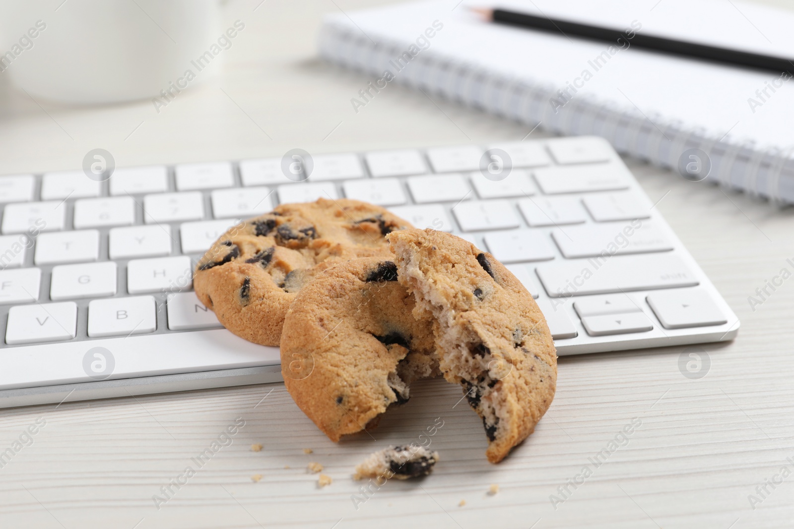 Photo of Chocolate chip cookies and keyboard on white wooden table, closeup