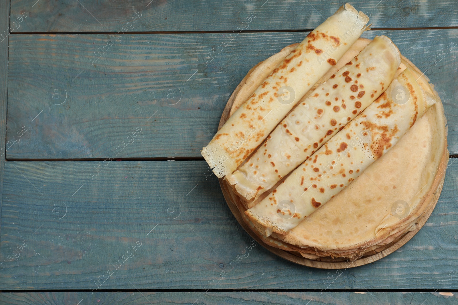 Photo of Delicious crepes on blue wooden table, top view. Space for text