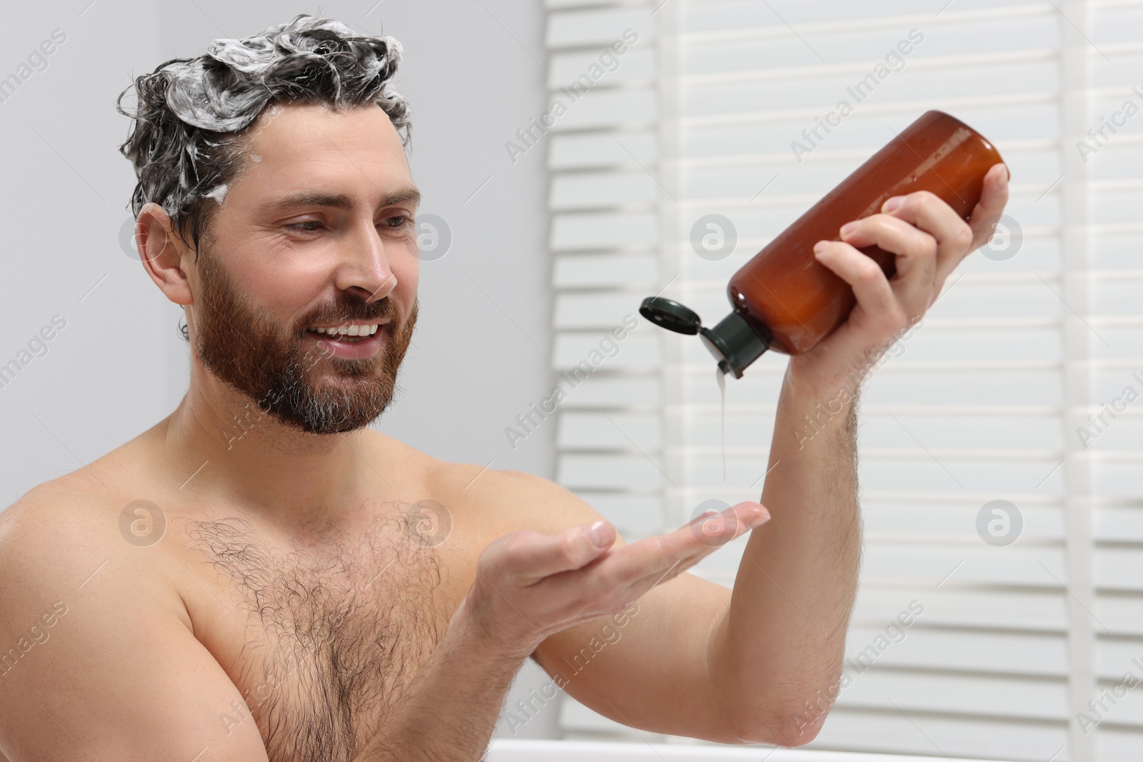 Photo of Happy man pouring shampoo onto his hand in shower