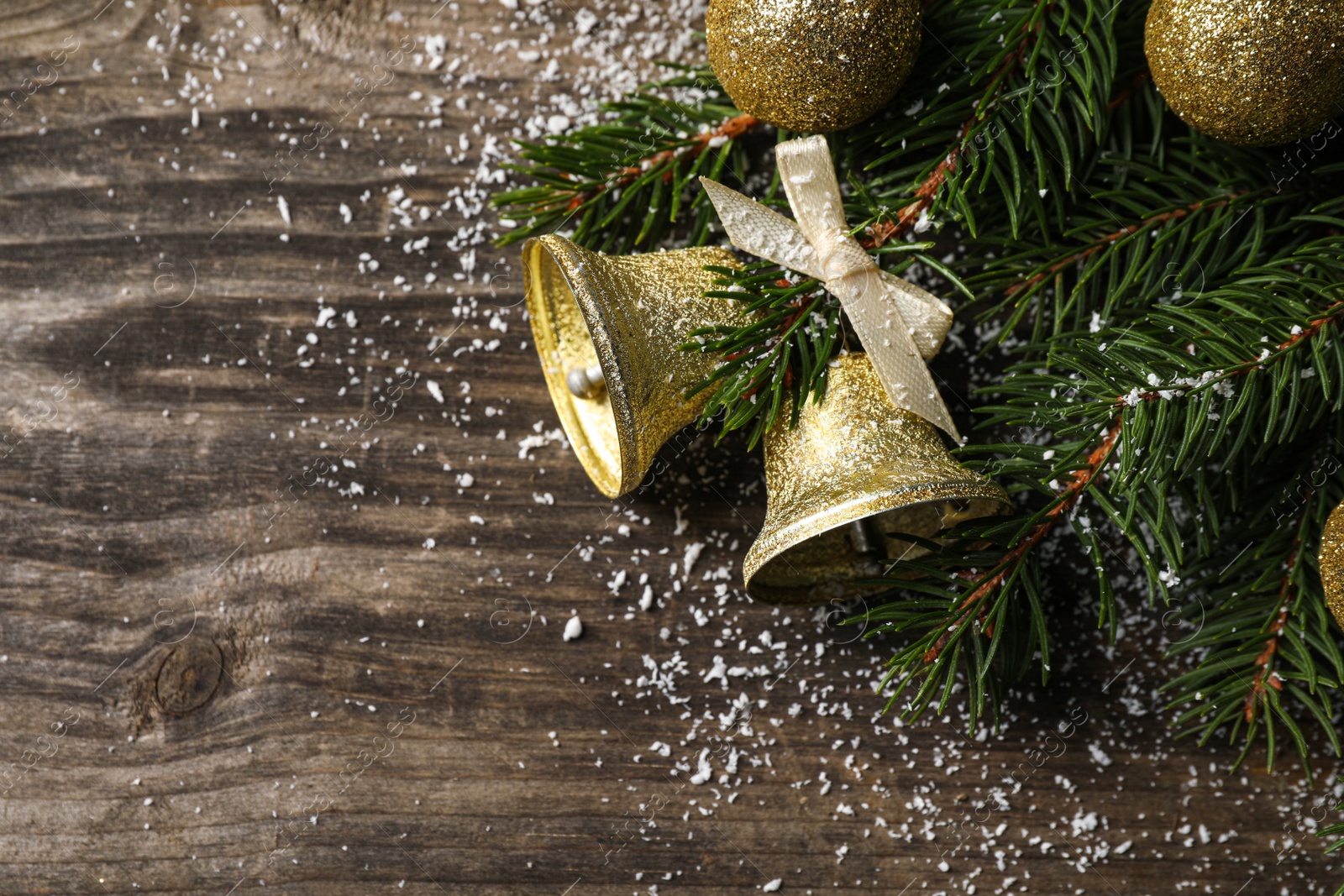 Photo of Christmas bells and fir tree branches with festive decor on wooden table, flat lay. Space for text