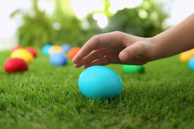 Little child taking Easter egg from green grass, closeup