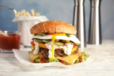 Photo of Tasty burger with fried egg on table against blurred background