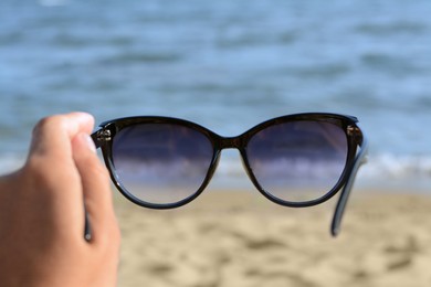 Woman holding stylish sunglasses near beautiful sea, closeup