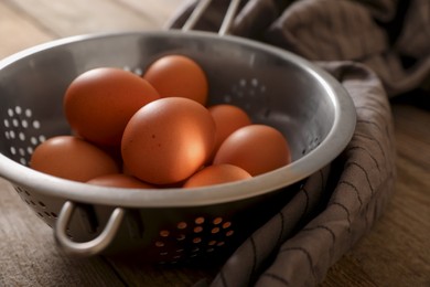 Photo of Chicken eggs in colander and napkin on wooden table