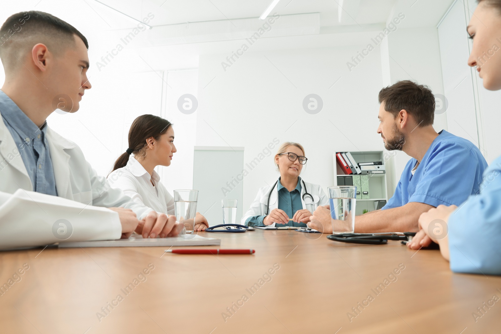 Photo of Medical conference. Team of doctors having discussion with speaker at wooden table in clinic